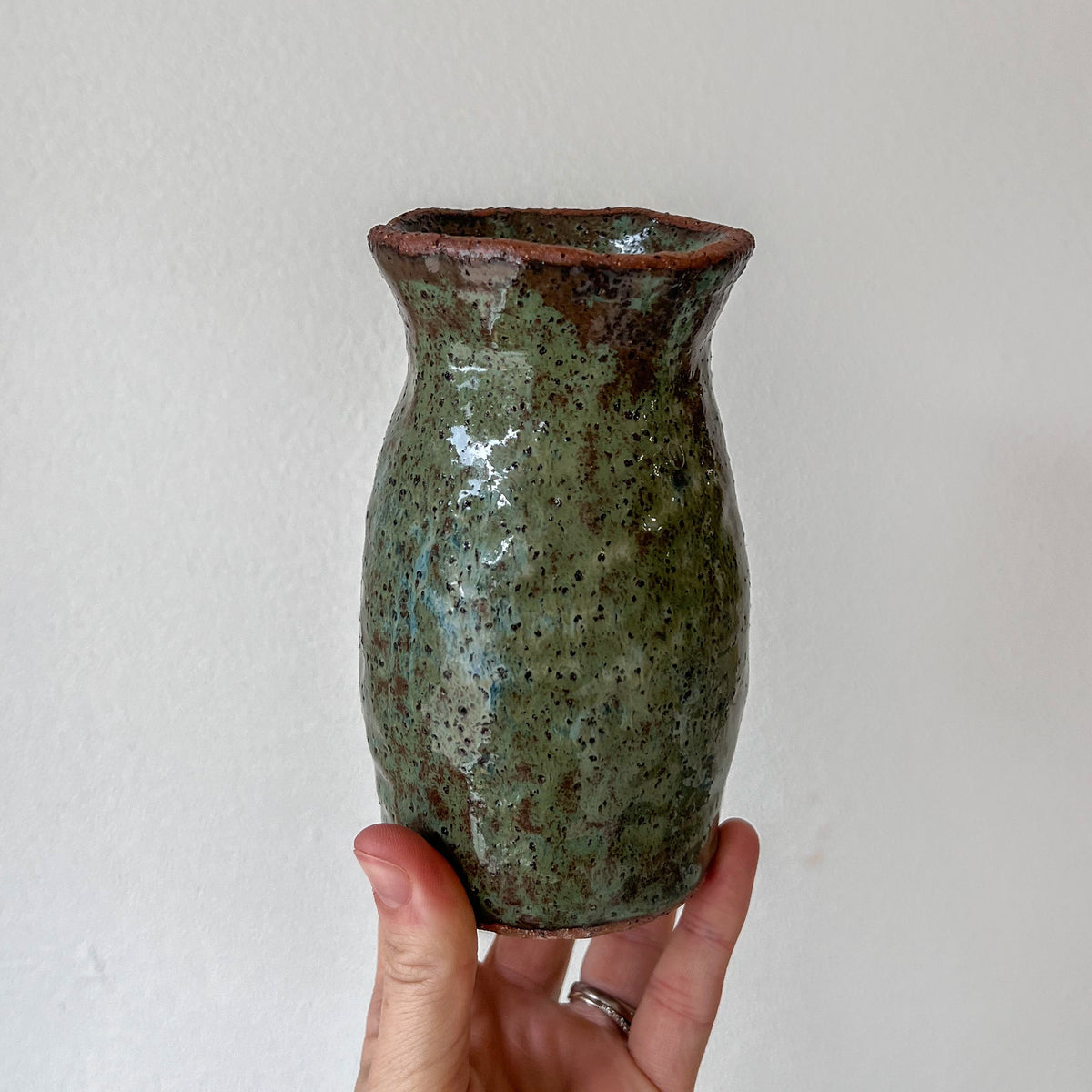 Hand holding a green ceramic vase against a plain background