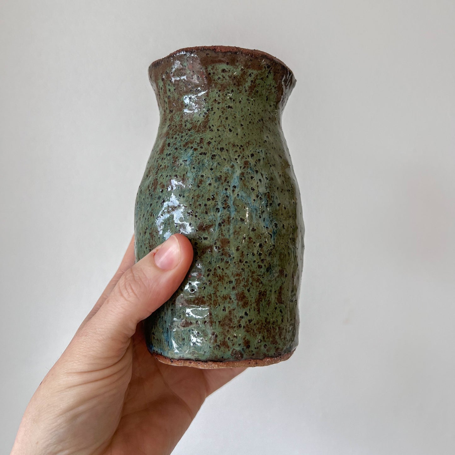 Hand holding a ceramic bottle with a speckled glaze against a plain background