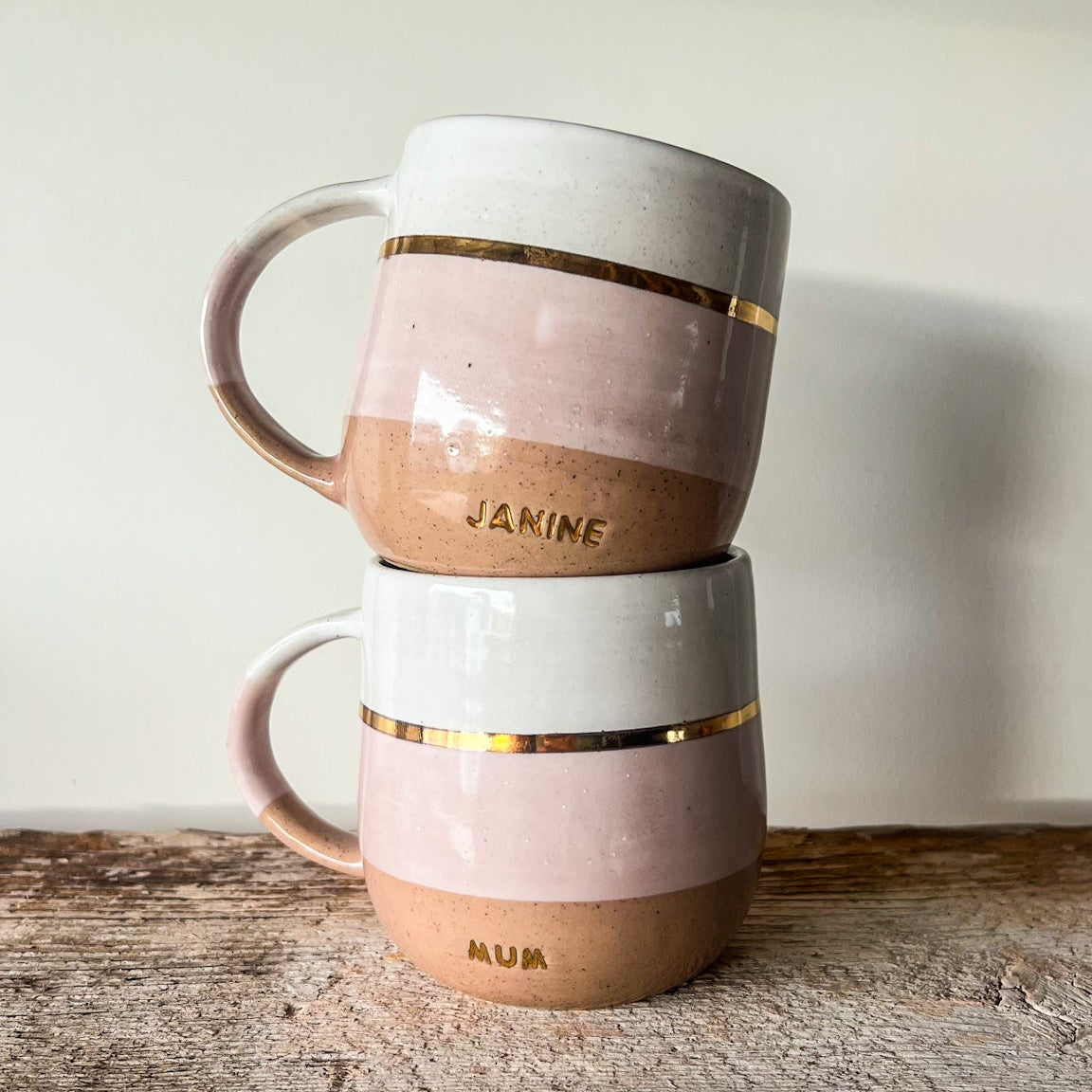 Stack of three ceramic mugs with gold accents on a wooden surface