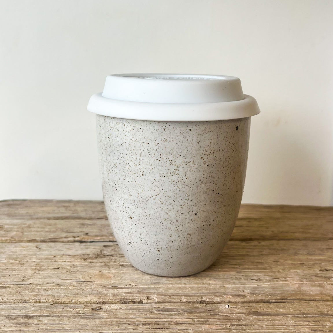 Speckled ceramic cup with a white lid on a wooden surface