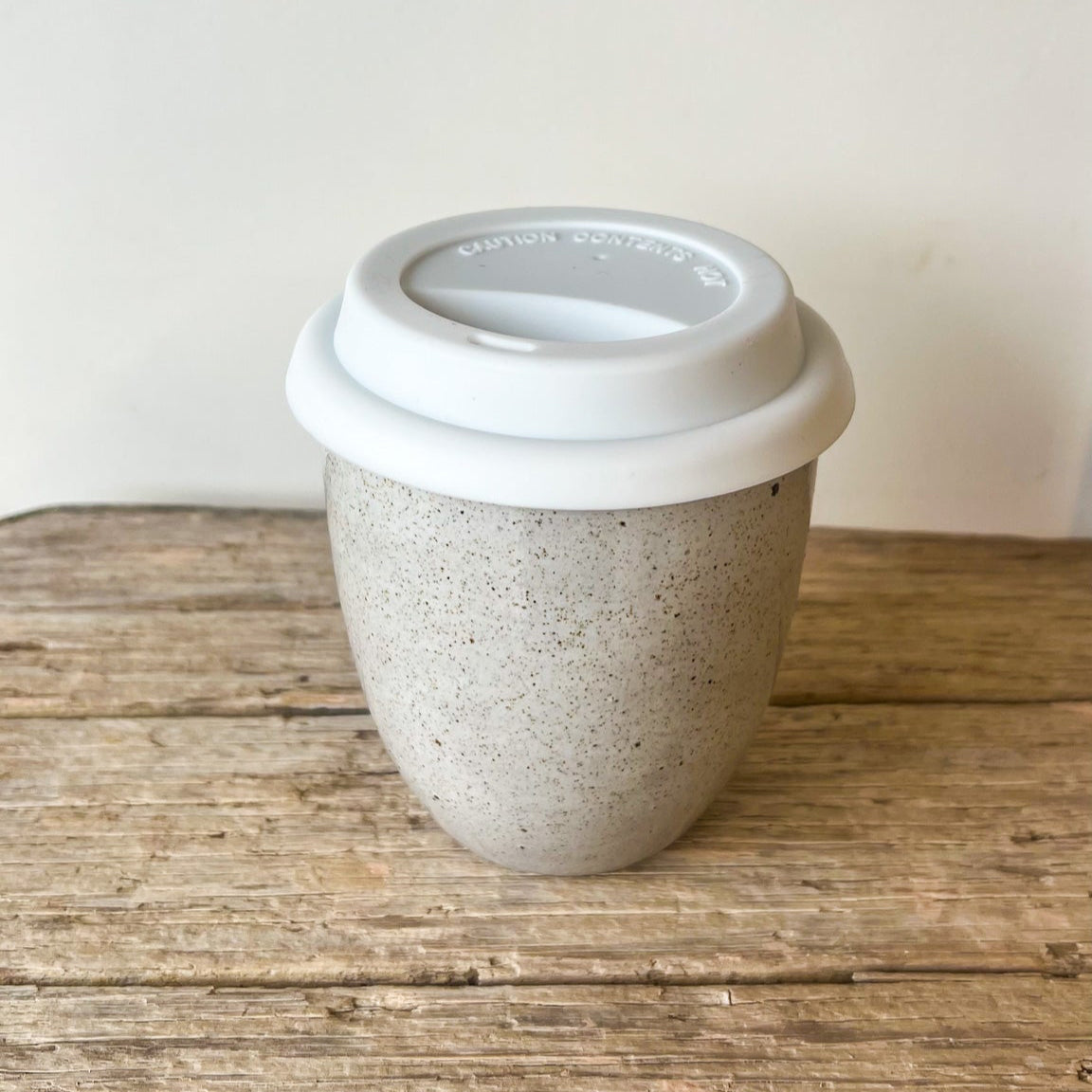 Reusable coffee cup with a white lid on a wooden surface