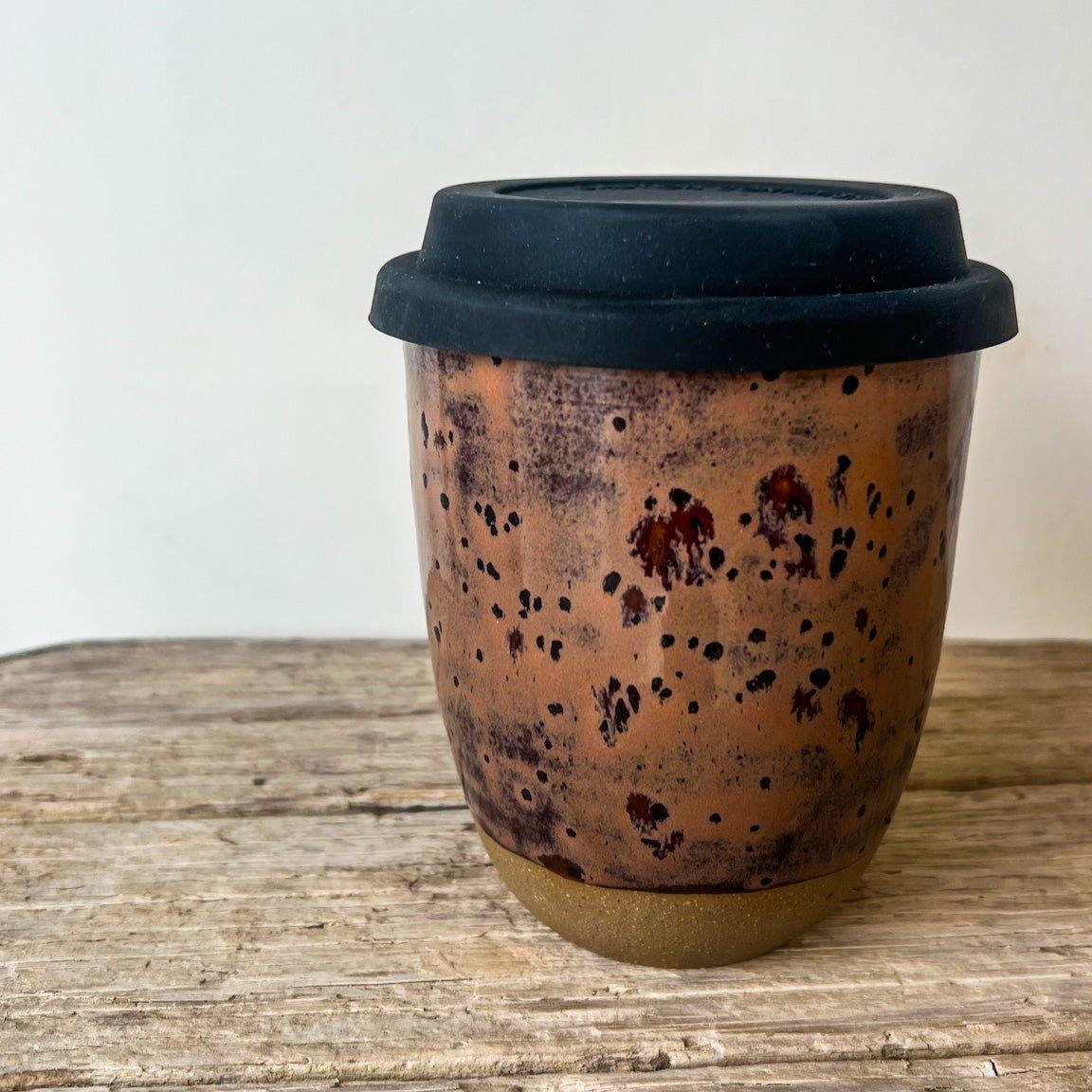 Ceramic coffee cup with black lid on a wooden surface