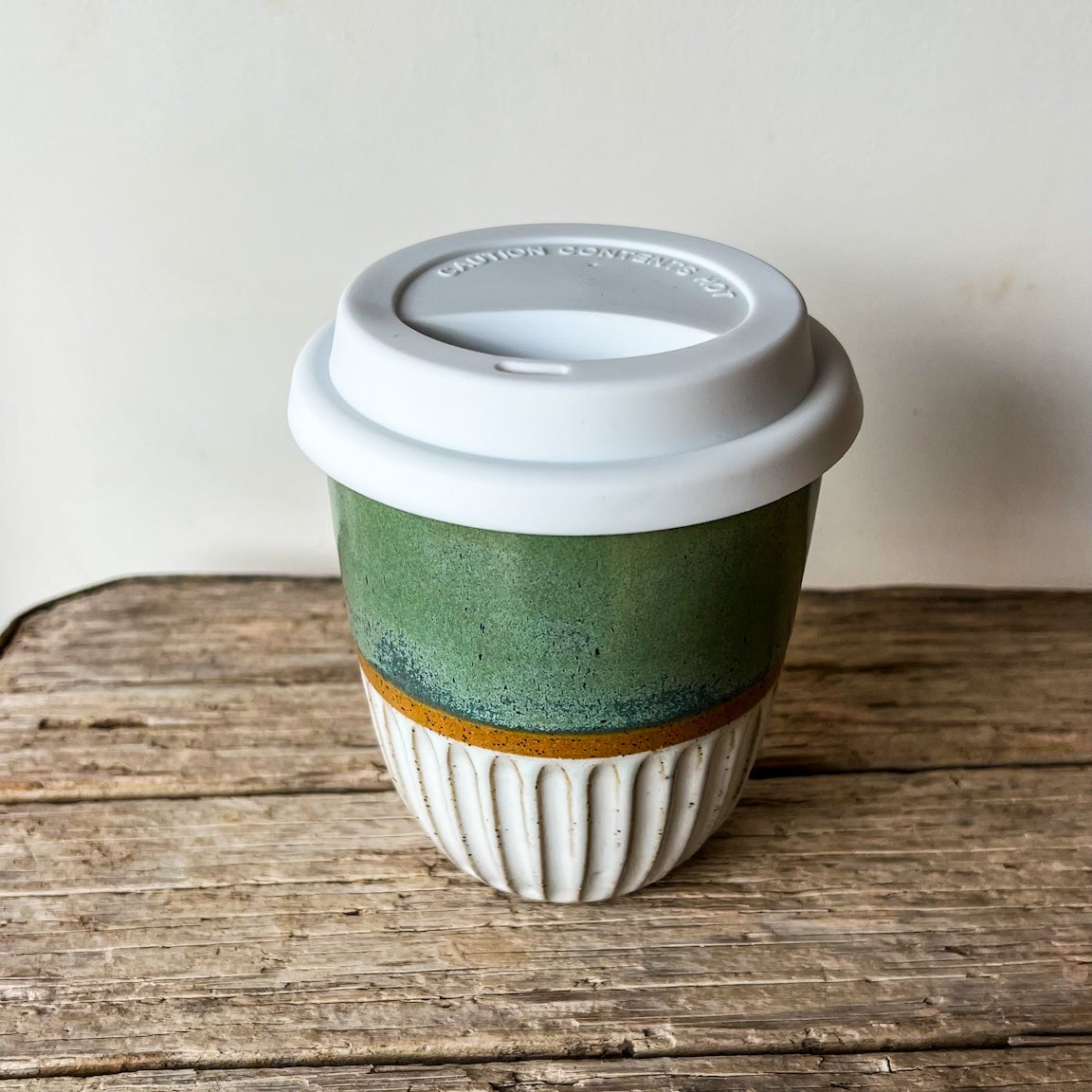 Green ceramic coffee cup with a white lid
