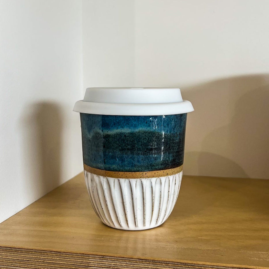 Ceramic cup with a blue pattern on a wooden shelf against a white wall.