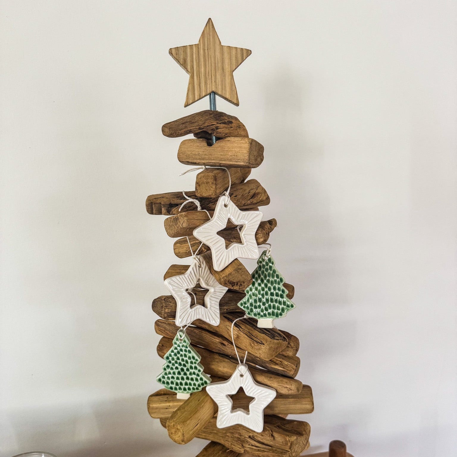 Wooden Christmas tree made from driftwood with star-shaped decorations on a plain background