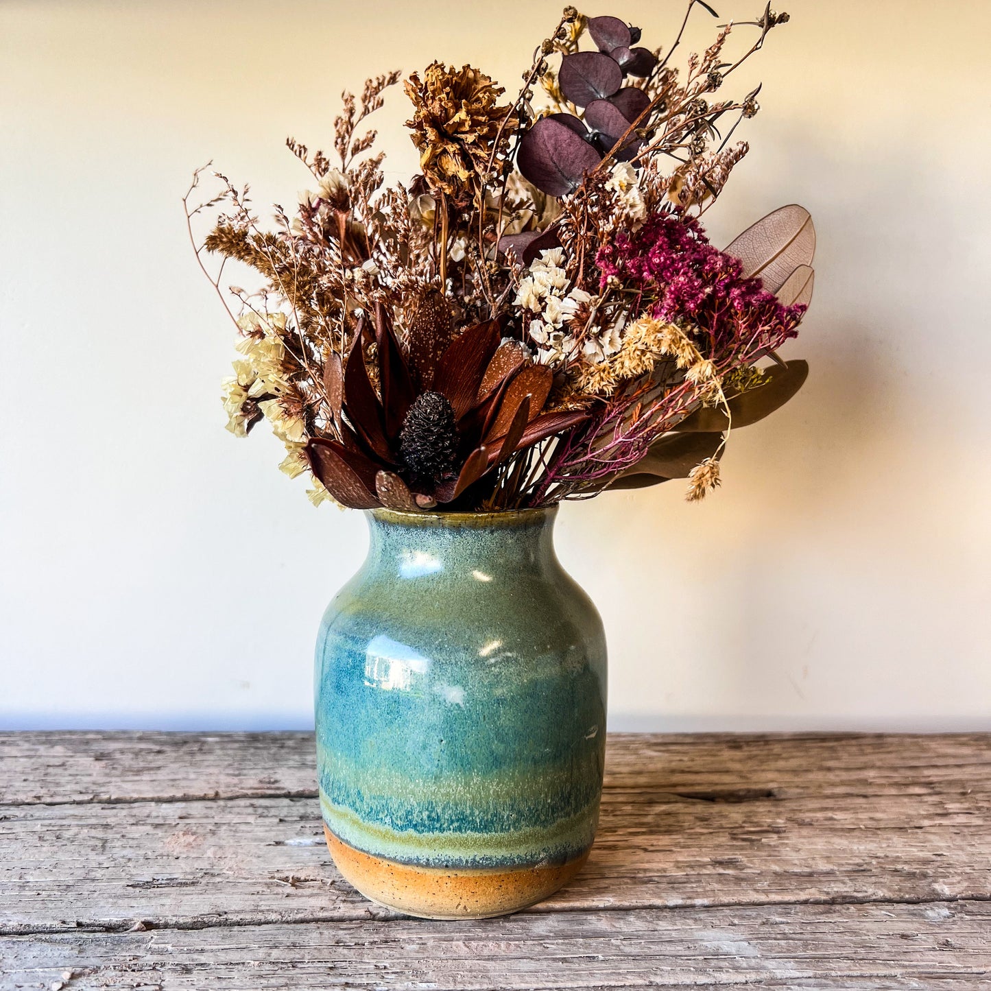 Small blue ceramic vase with dried flowers on a wooden surface