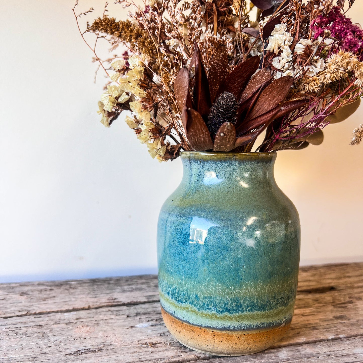Blue ceramic vase with dried flowers on a wooden surface