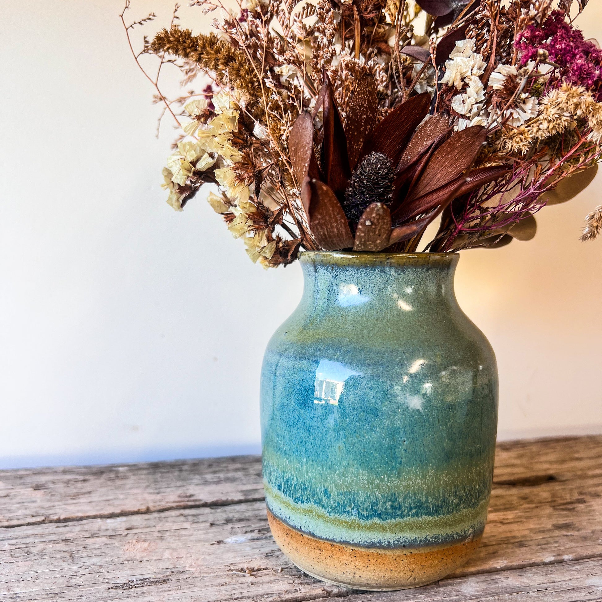 Blue ceramic vase with dried flowers on a wooden surface