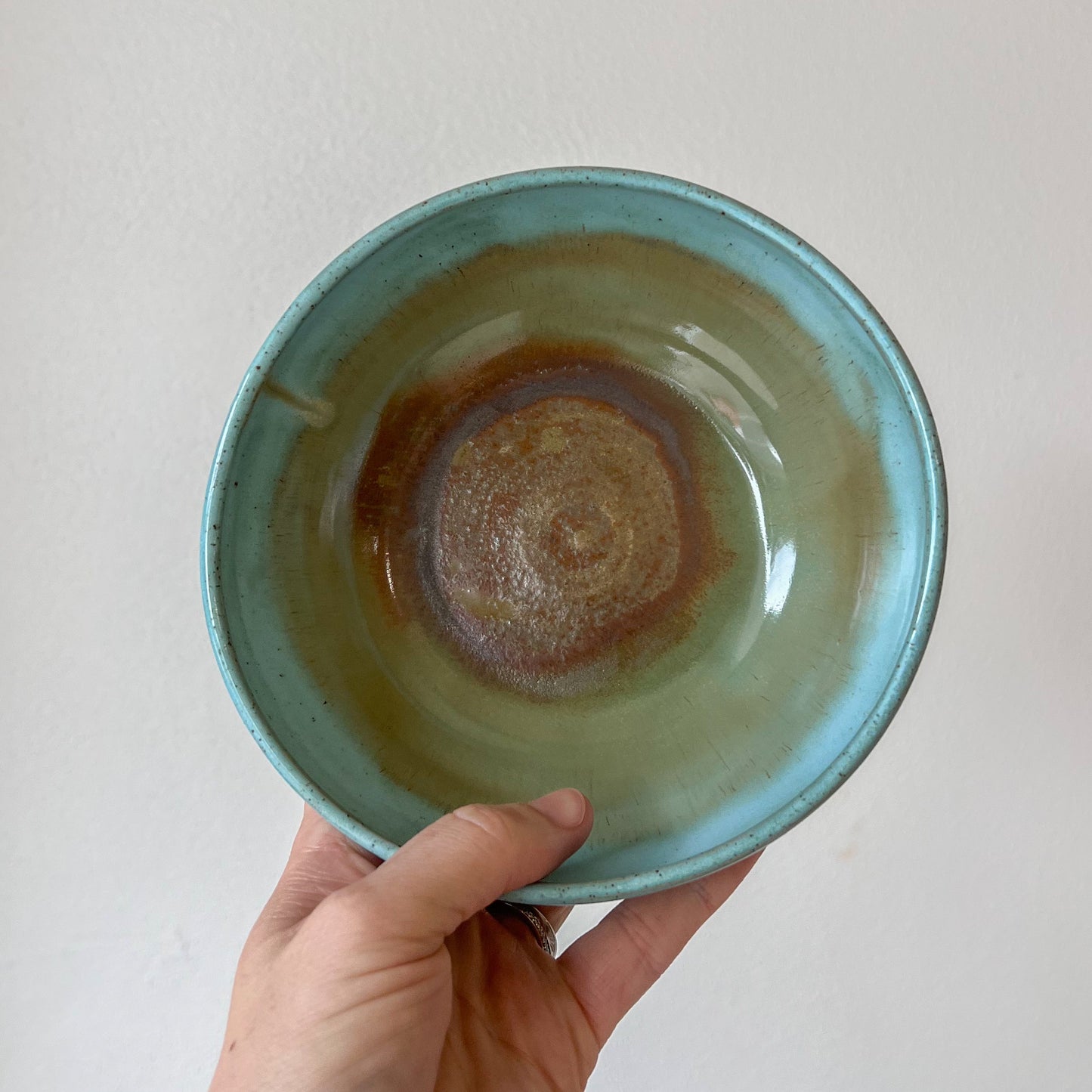 Hand holding a ceramic bowl with a gradient from green to brown against a plain background