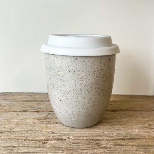 Speckled ceramic cup with a white lid on a wooden surface
