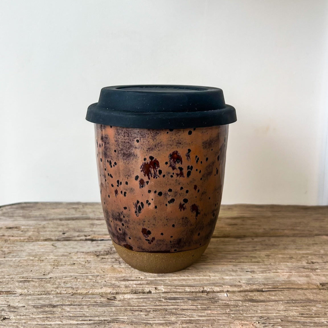 Ceramic cup with black lid on a wooden surface
