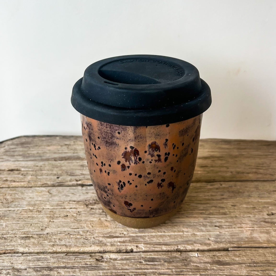 Copper travel mug with black lid on a wooden surface
