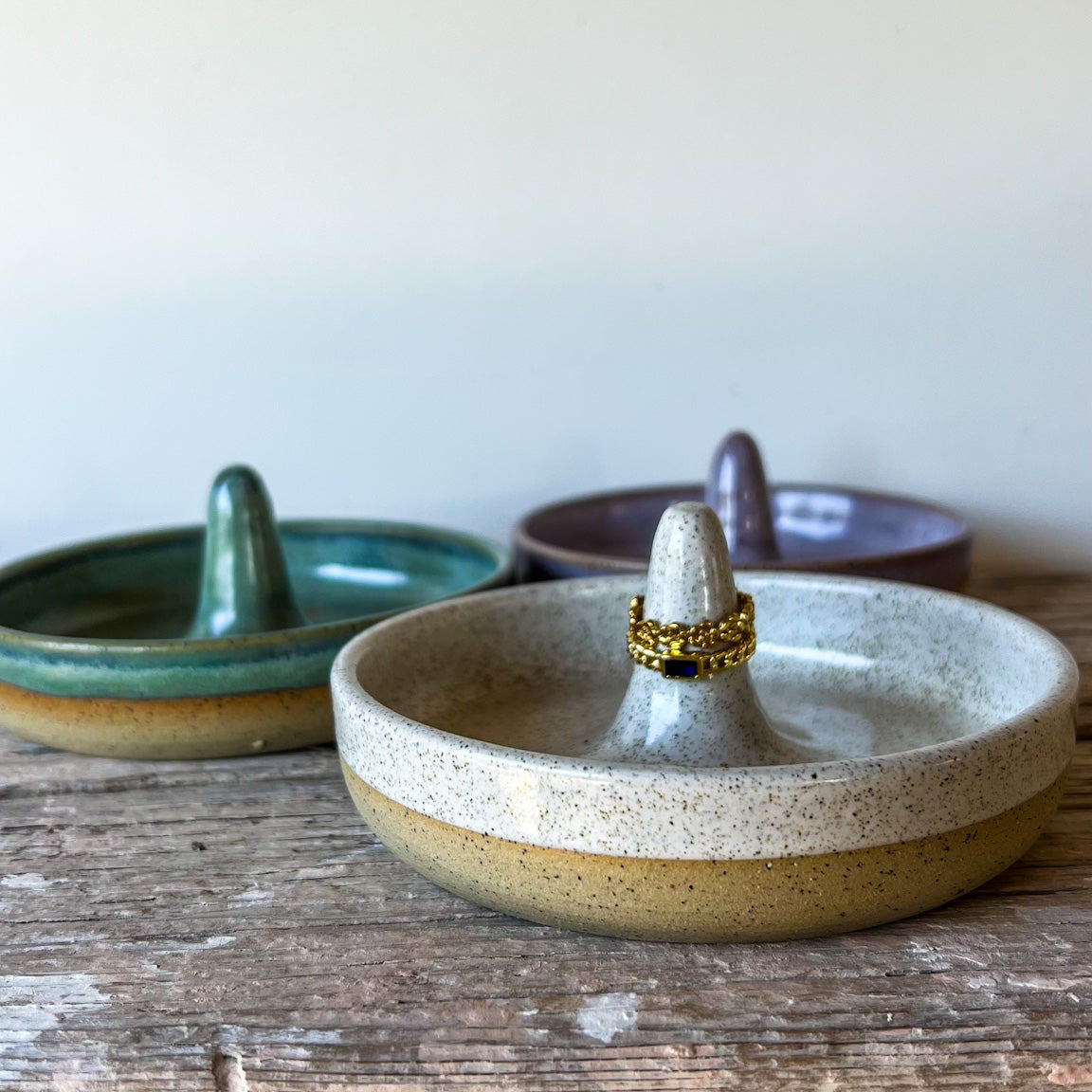 Three ceramic ring holders on a wooden surface with a white background