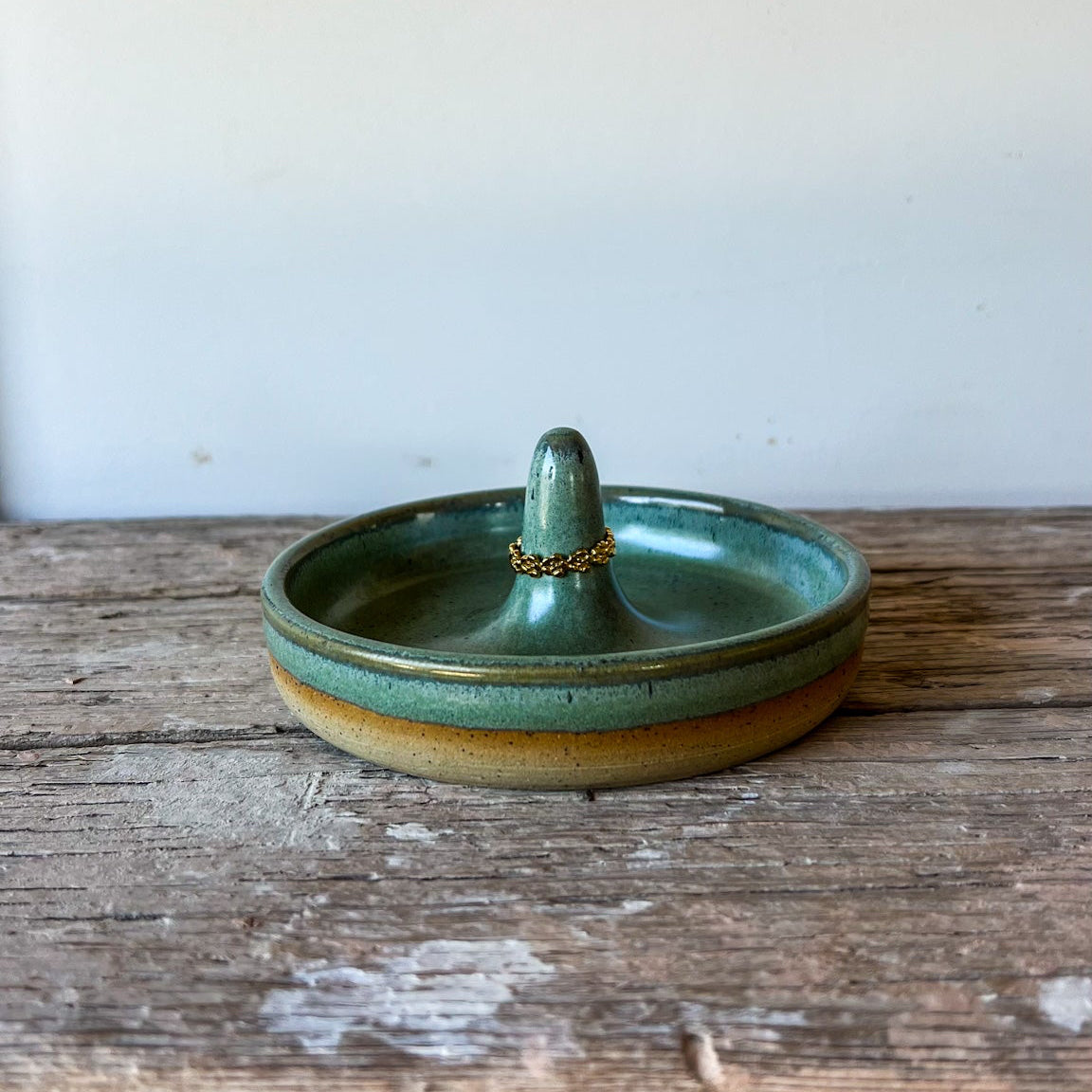 Green ceramic ring holder on a wooden surface with a white background