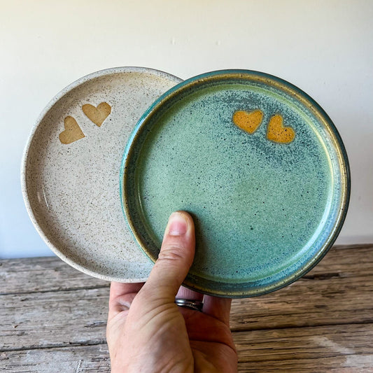 Hand holding a green ceramic plate with heart designs on a wooden surface