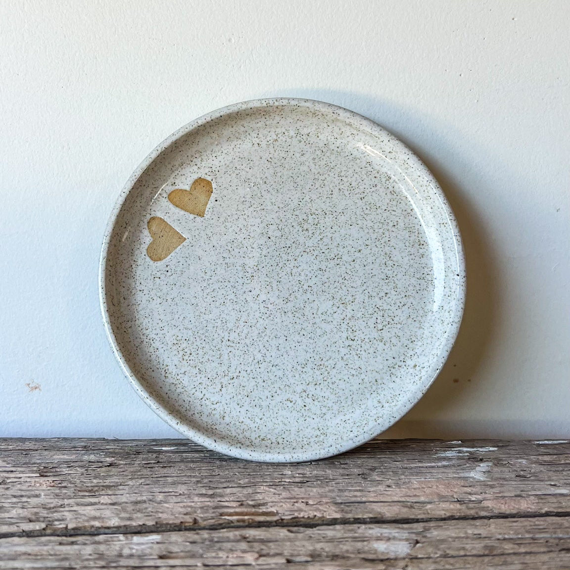 Speckled ceramic plate with two gold hearts on a wooden surface and light background