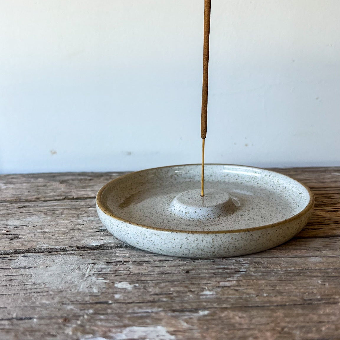 Incense stick in a ceramic holder on a wooden surface with a white background