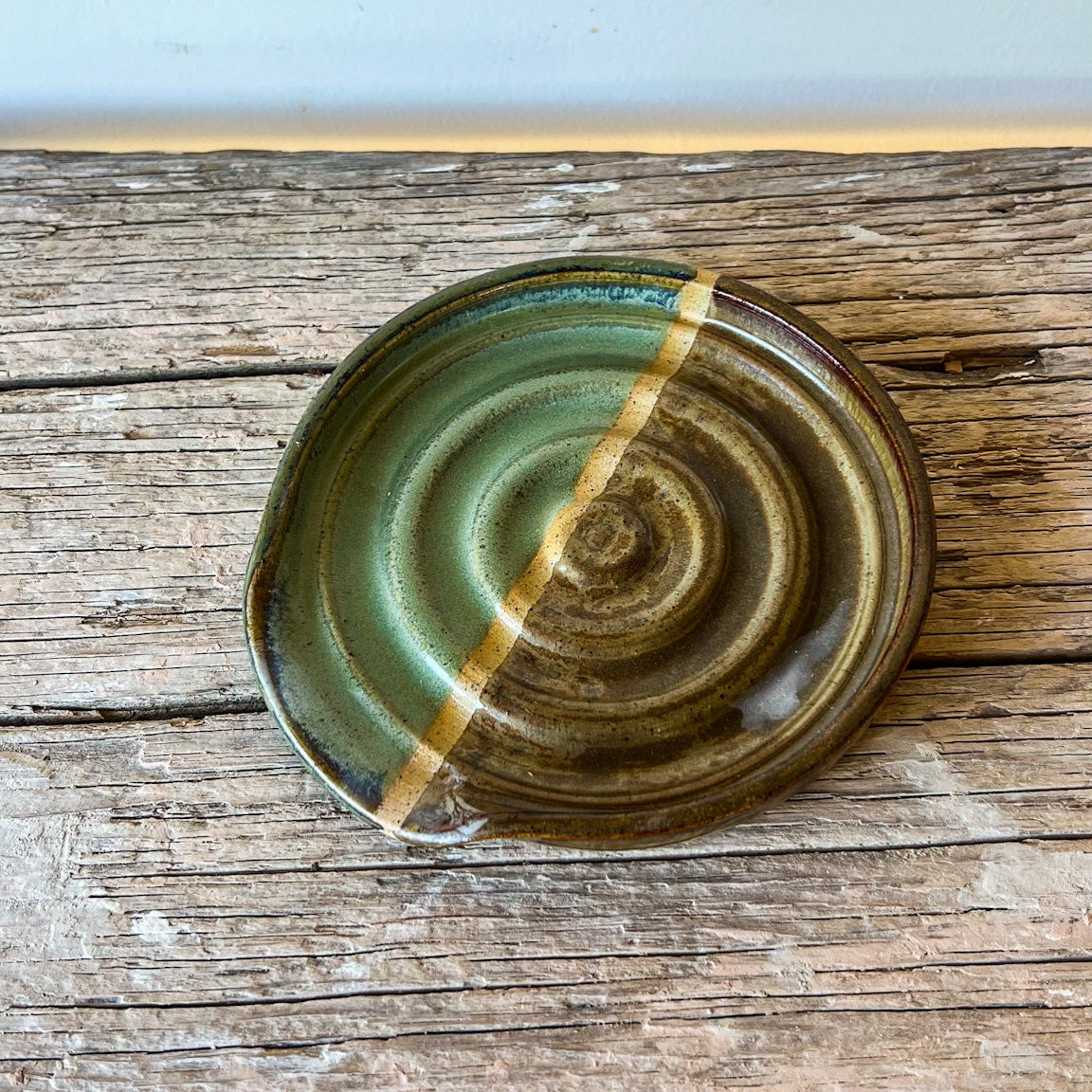 Ceramic dish with green and brown glaze on a wooden surface