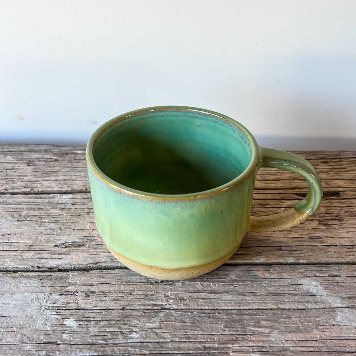 Green ceramic mug on a wooden surface with a white background
