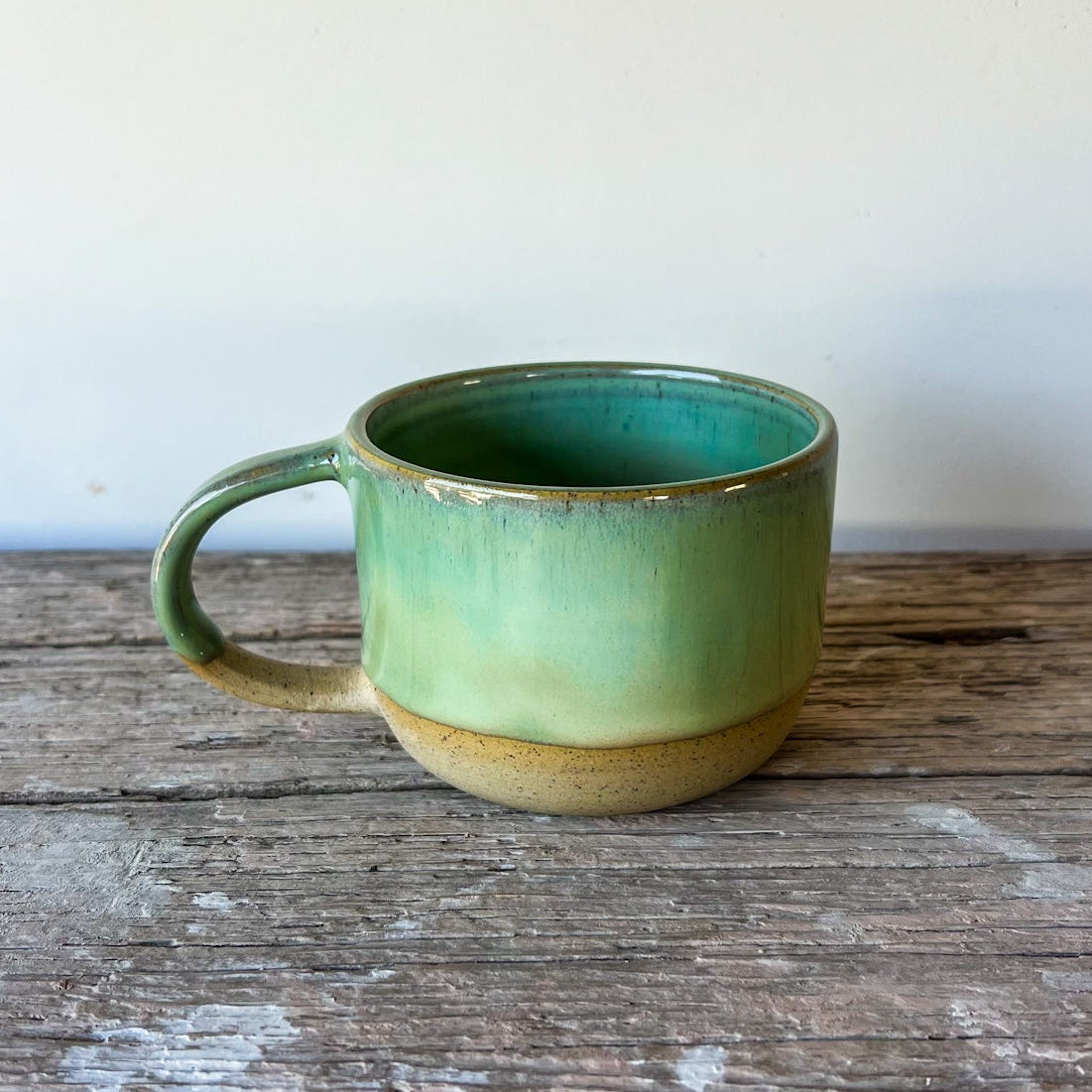Green ceramic mug on a wooden surface with a white background