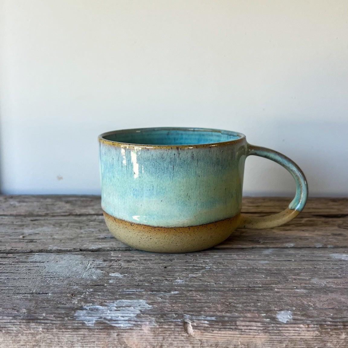 Ceramic mug with a greenish-blue glaze on a wooden surface