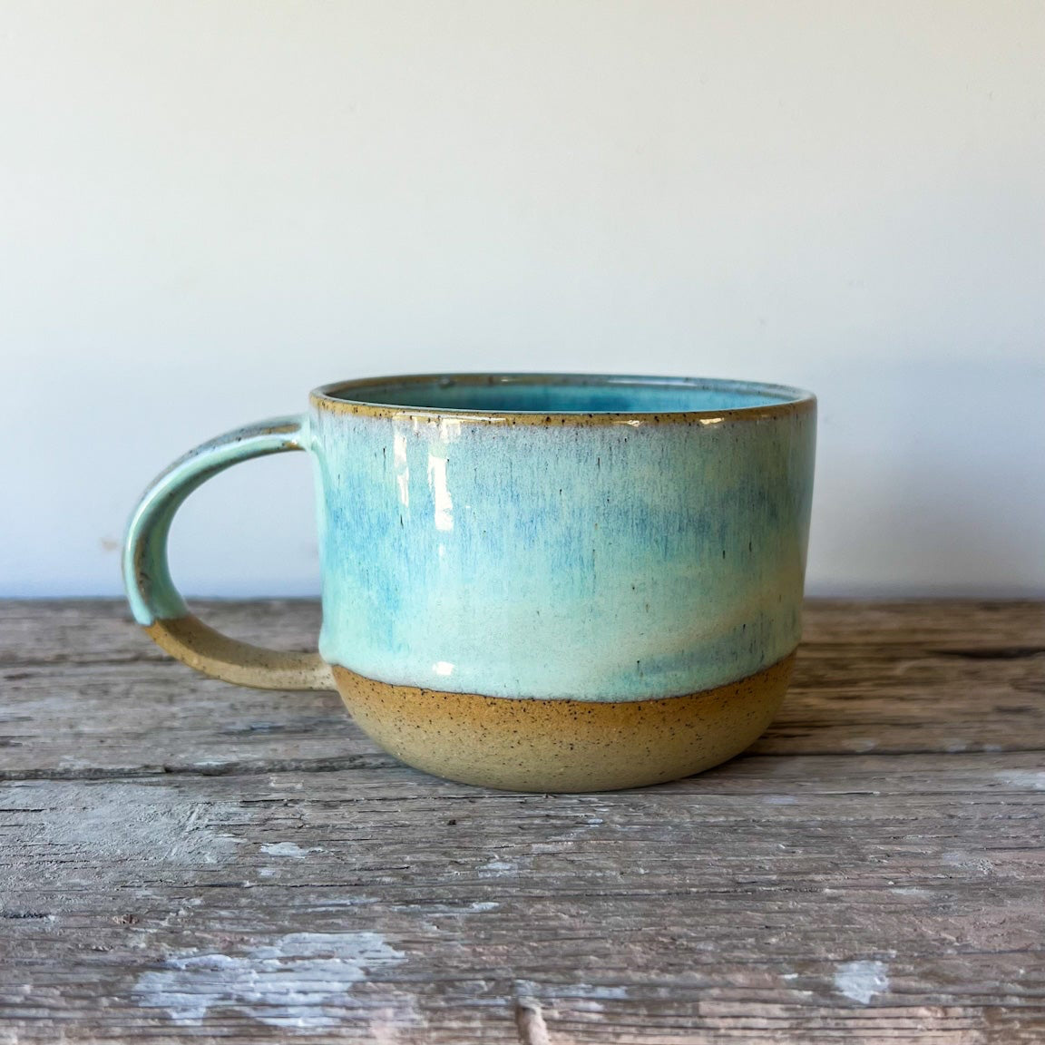 Ceramic mug with a blue-green glaze on a wooden surface