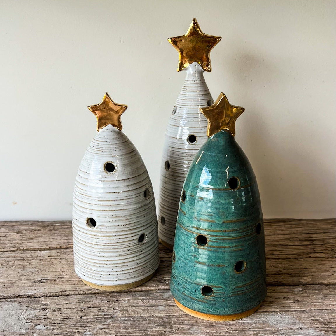 Three ceramic Christmas trees with star decorations on a wooden surface.