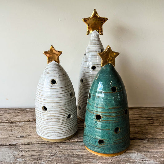 Three ceramic Christmas trees with star decorations on a wooden surface.