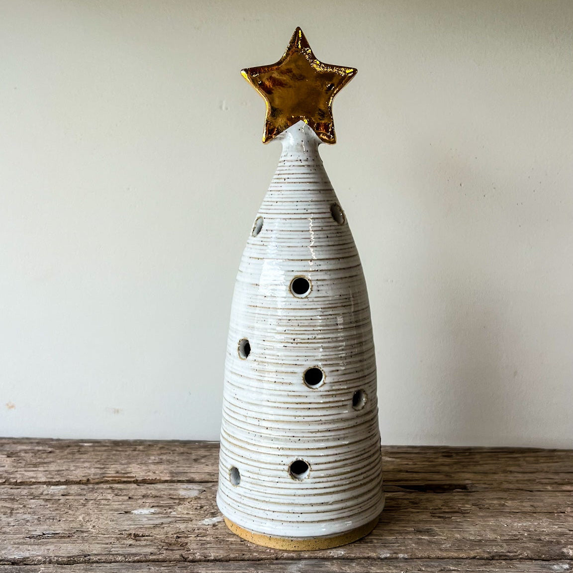 Ceramic Christmas tree with a gold star on top, placed on a wooden surface.