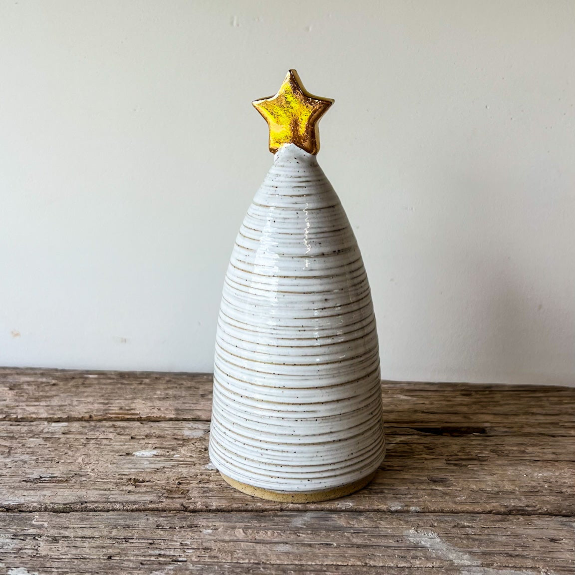 Ceramic Christmas tree with a gold star on top, placed on a wooden surface.