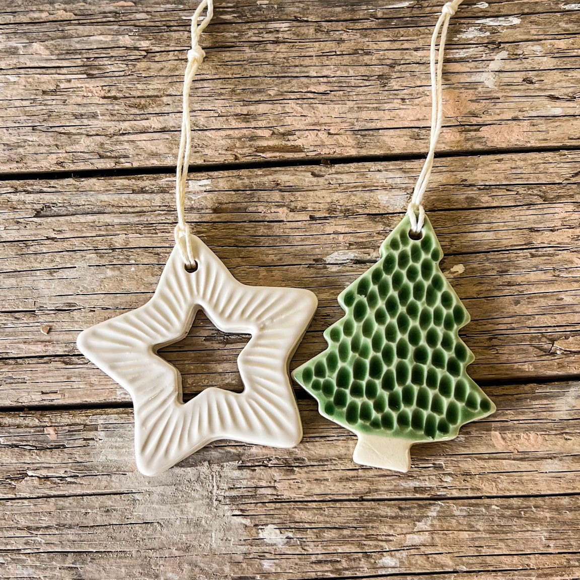 Two ceramic ornaments, one star-shaped and one tree-shaped, on a wooden surface.